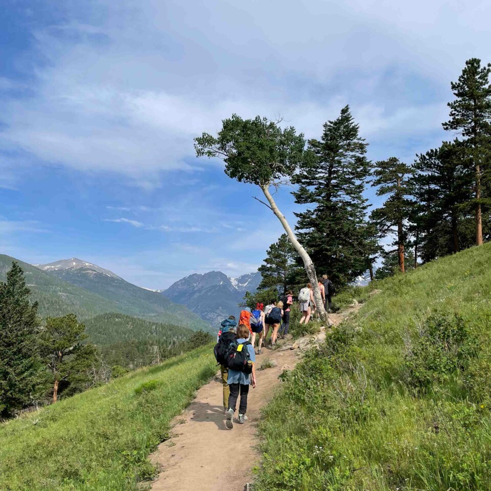 Line of campers hiking up path in mountains.