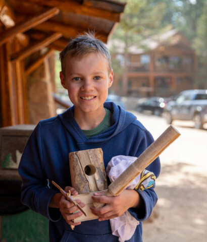 Boy smiling holding wood.