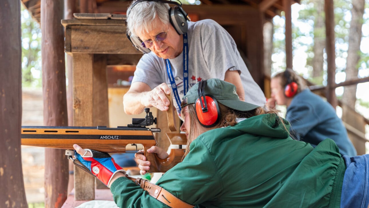 Man helping girl shoot rifle.