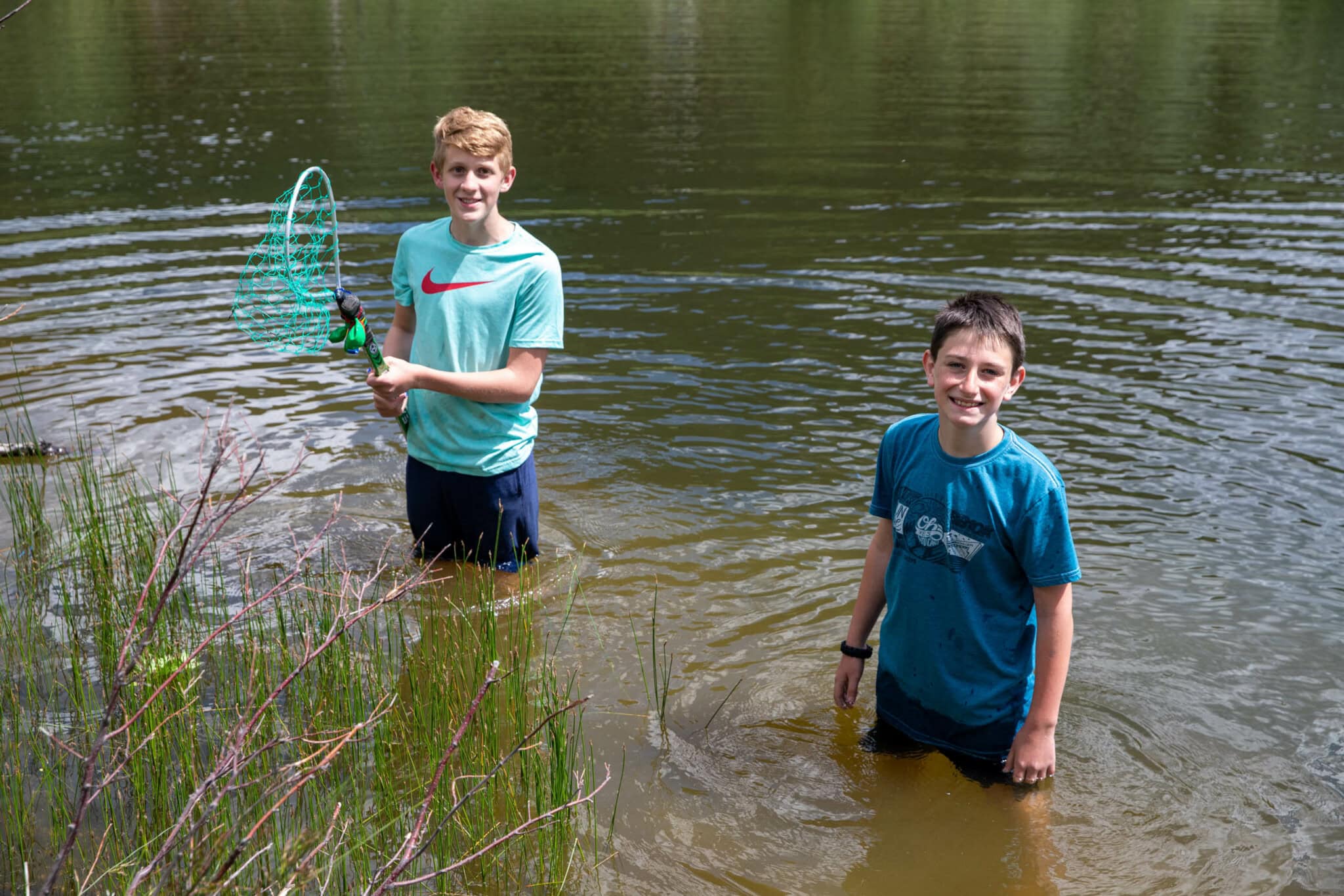 Campers wading in a river with a fishing net.