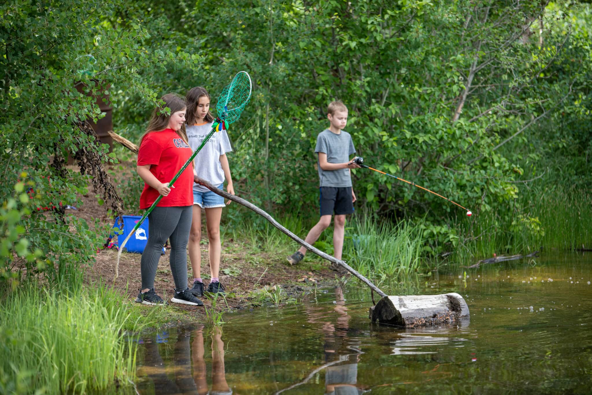Campers on the riverbank with fishing nets and poles.