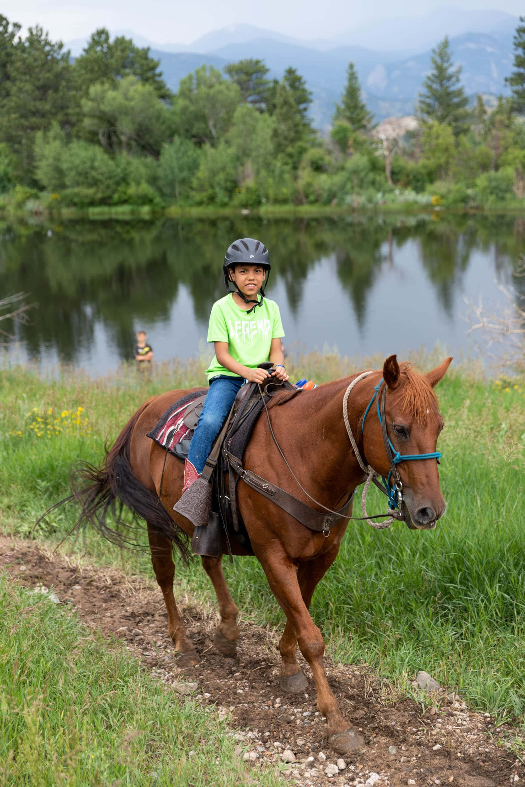 Camper on a horse on a trail by a lake.
