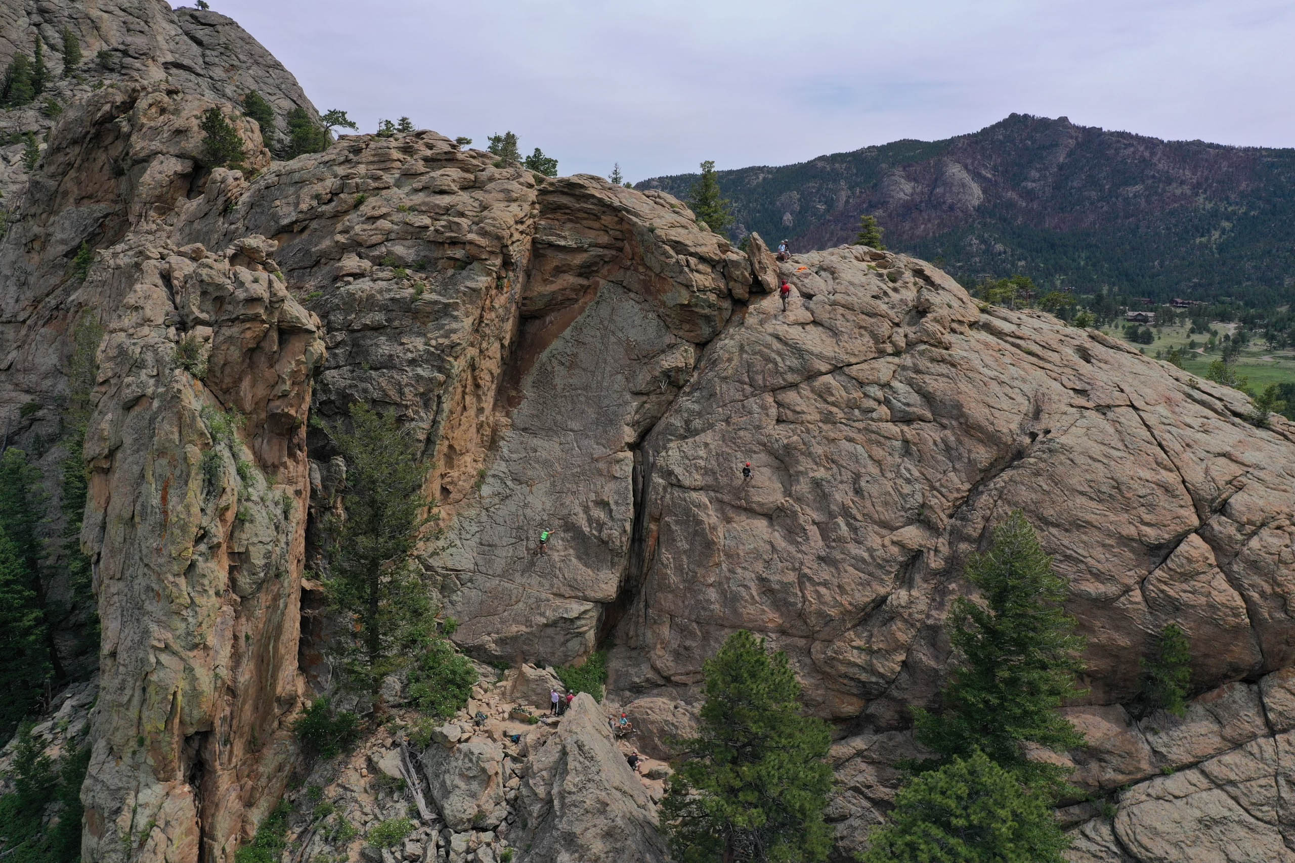 Campers doing technical rock climbing on a big rock face.