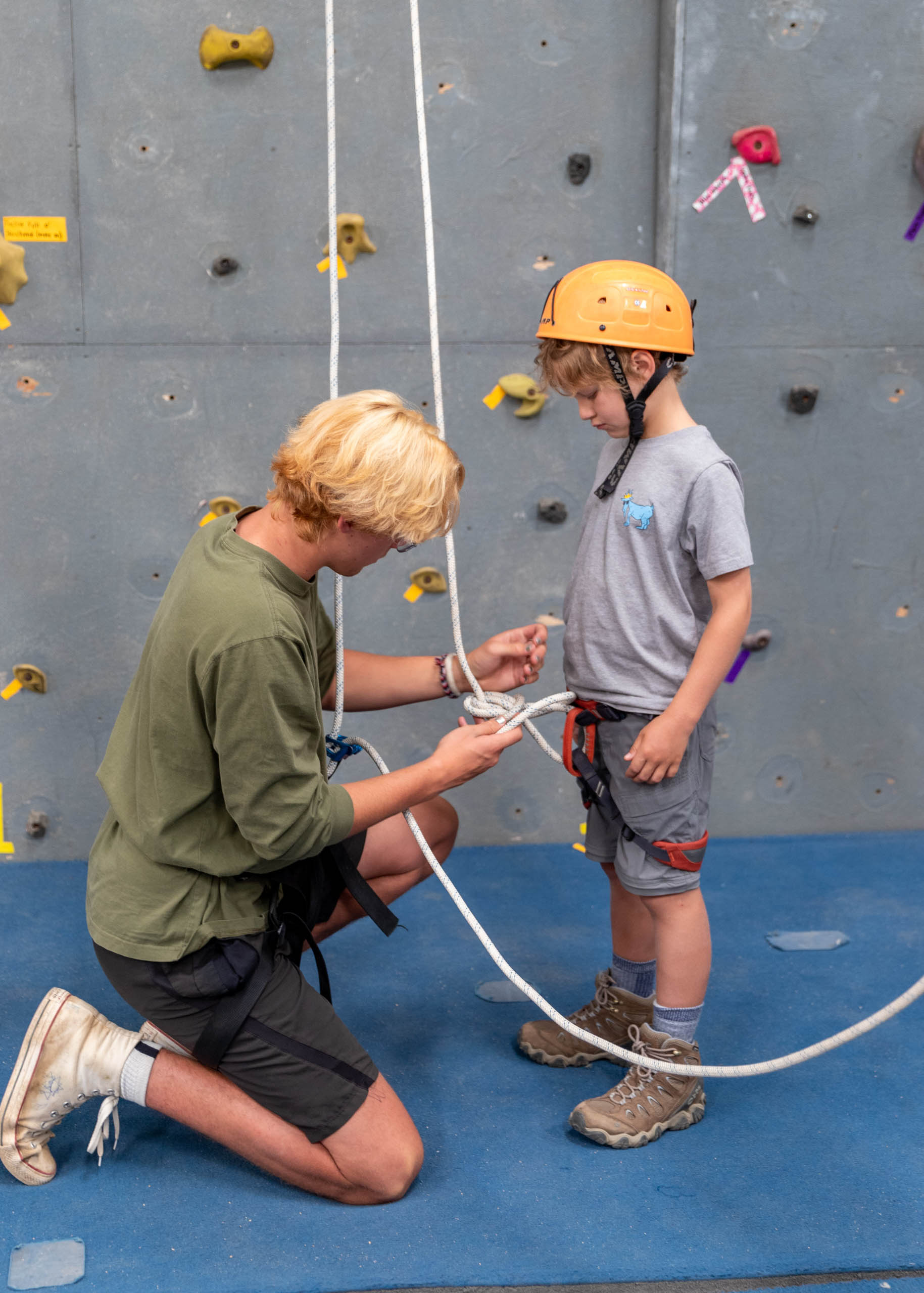 Counselor tying a camper into the ropes for the rock wall.